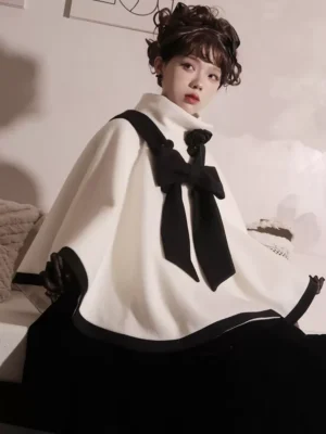 Right side profile view of burgundy and cream Rococo Lolita cape coat featuring large black velvet bow at neckline, structured shoulders, and black fabric trims on model with vintage hairstyle