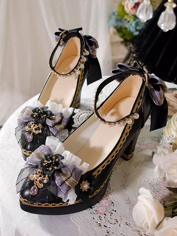 Gothic Lolita platform pumps with deep blue fabric bows and golden embroidered trim displayed on ornate lace table with decorative flowers and jeweled accents