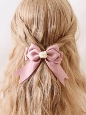 Sweet lolita pink bow headdress with rose ornament worn on model with blonde wavy hair in half-up hairstyle, rear view showing double-layer satin bow and fishtail ribbons, rococo-inspired romantic aesthetic