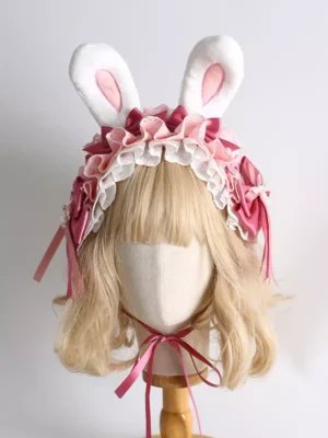 Pink and white plush bunny ear lolita headdress with ruffled lace trim and burgundy satin bow, displayed on blonde wig mannequin head, frontal flat view showing full design