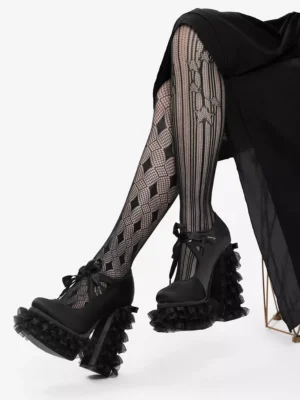 Black gothic lolita platform pumps with lace-up bow detail, shown on model wearing black outfit and patterned tights, featuring ruffled platform sole and chunky block heel from mixed side and frontal angle