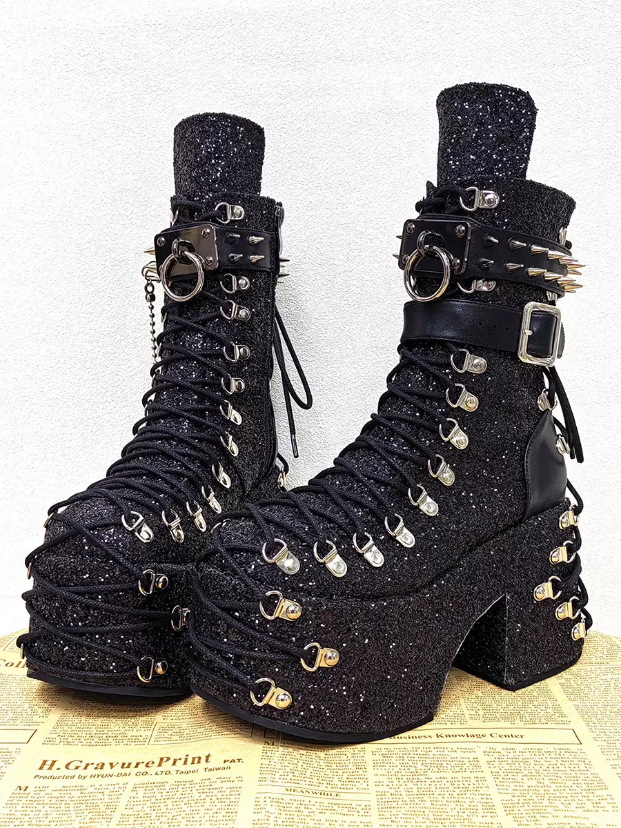 Gothic lolita platform boots front oblique view with newspaper print background featuring side hanging chain decorations, spiked buckle strap, black glitter fabric, and silver lace hardware