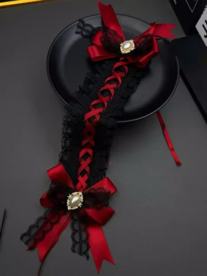 Gothic lolita pearl bow headpiece featuring red satin cross-shaped bows, intricate black lace trim, and gold-tone pearl brooches displayed in top-down flat lay on black ceramic plate