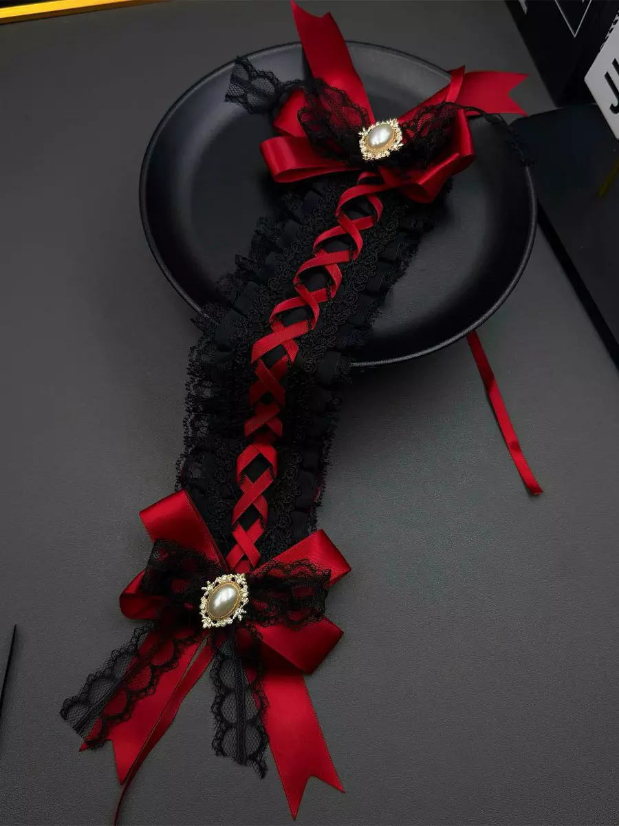 Gothic lolita pearl bow headpiece featuring red satin cross-shaped bows, intricate black lace trim, and gold-tone pearl brooches displayed in top-down flat lay on black ceramic plate
