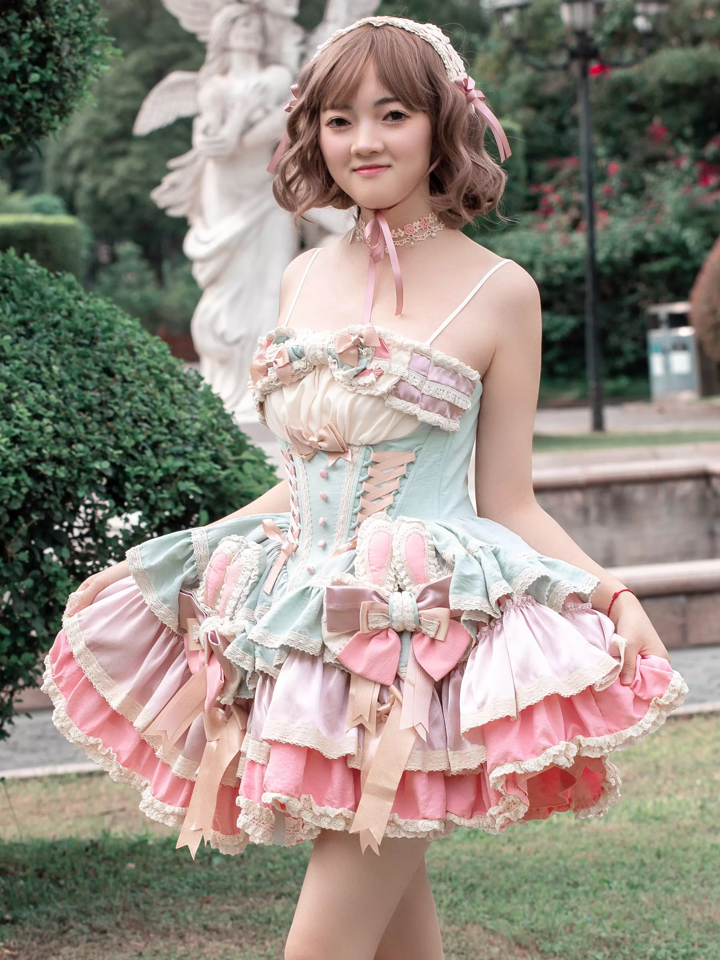 Medium outdoor photo of female model in pastel blue-pink sweet lolita dress with spaghetti straps waist bow decorations garden setting