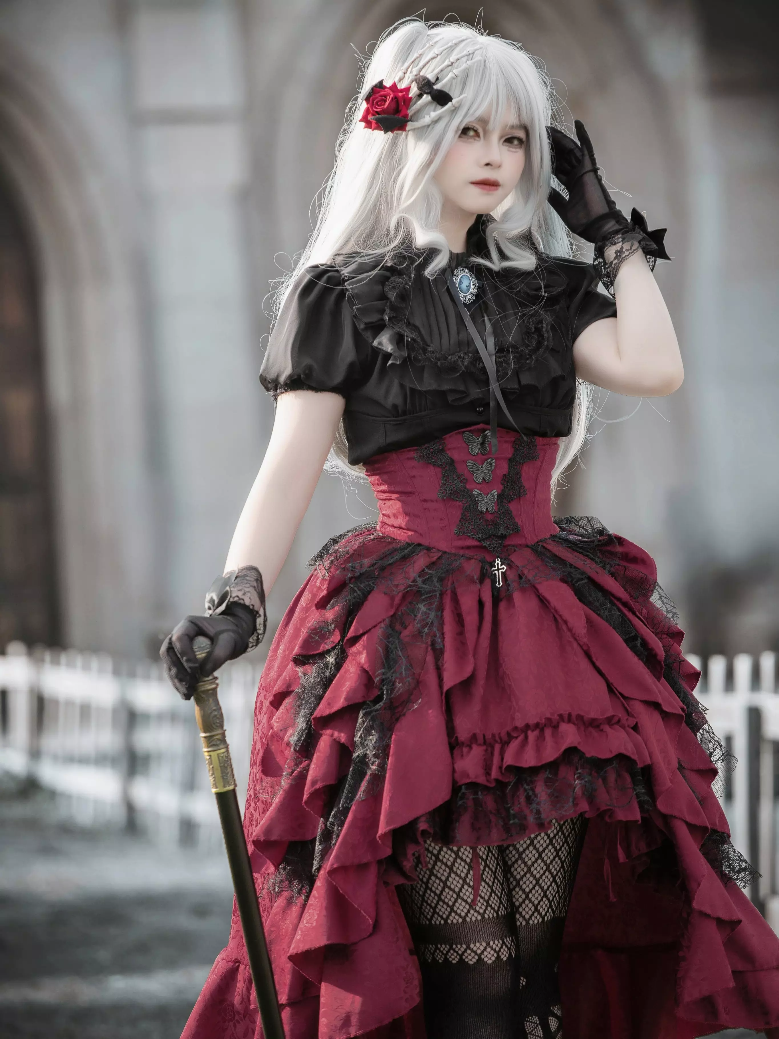 Gothic lolita dress set back three-quarter view with black lace blouse, wine-red high-low ruffle skirt, fishnet stockings and rose hair accessory