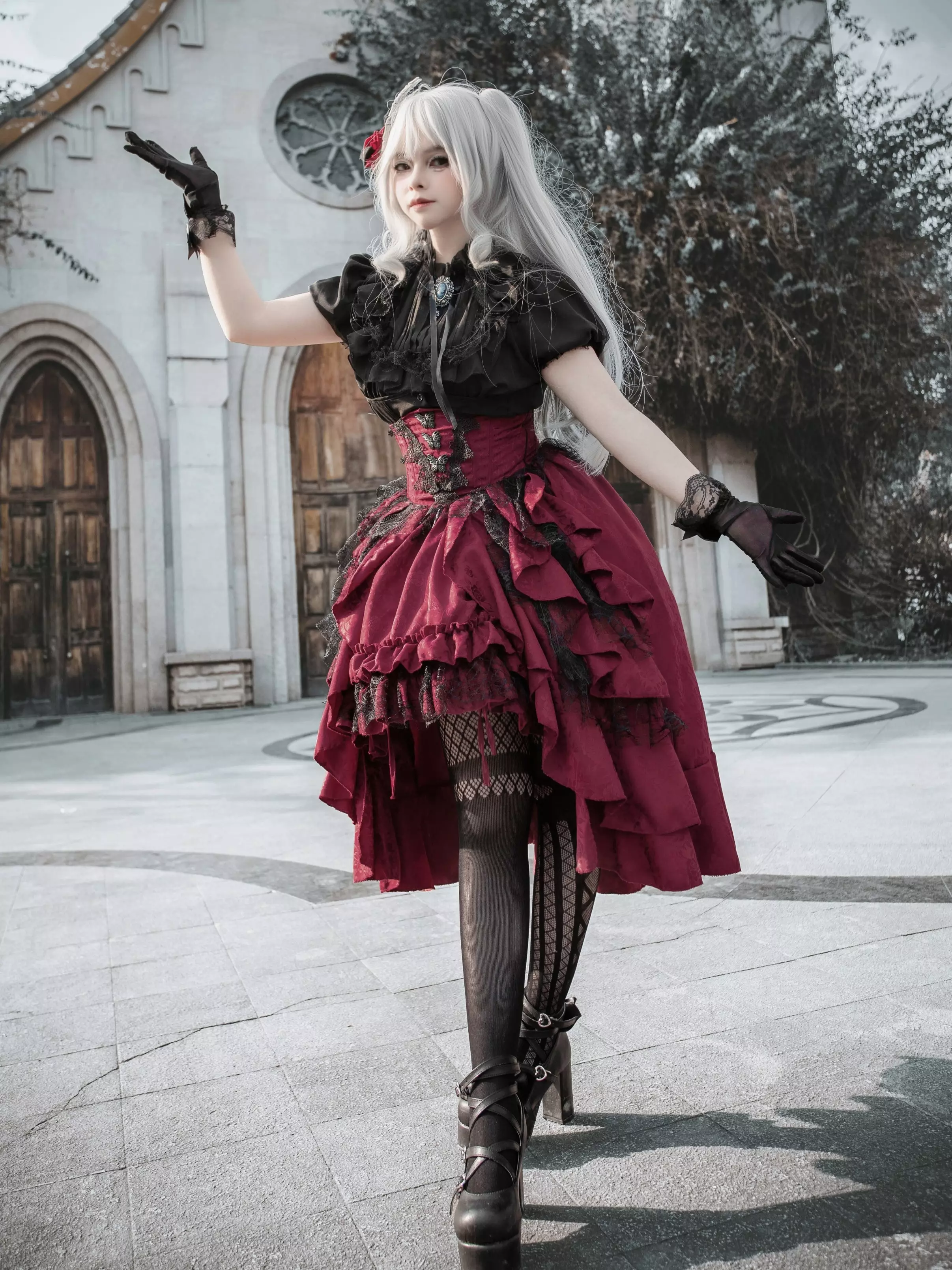 Gothic lolita ensemble featuring black lace blouse with puff sleeves, wine-red layered asymmetrical ruffle skirt, three-quarter side angle