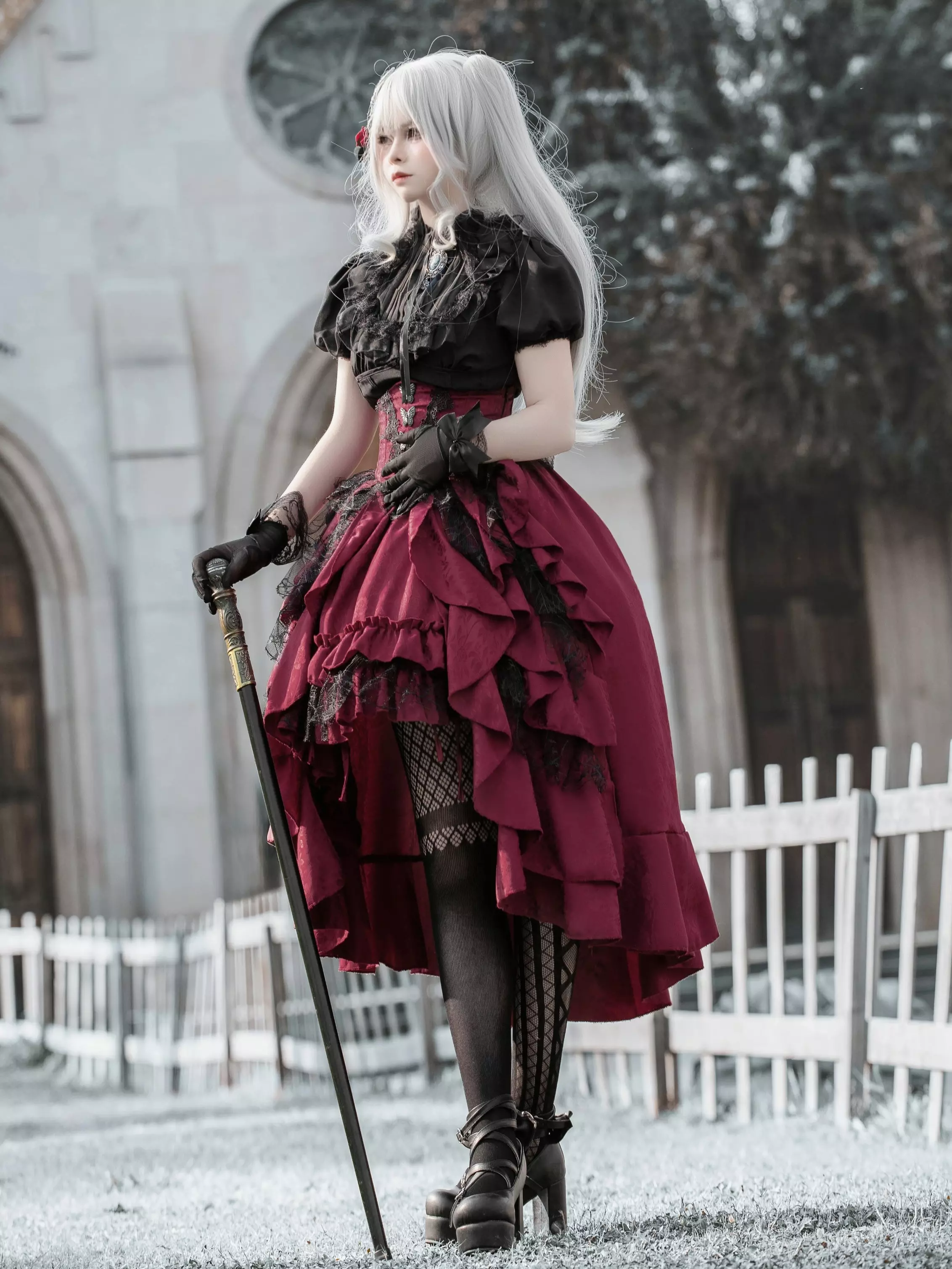 Gothic lolita fashion set with black lace blouse, wine-red tiered high-low ruffle skirt, fishnet hosiery, side angle showcasing volume and construction