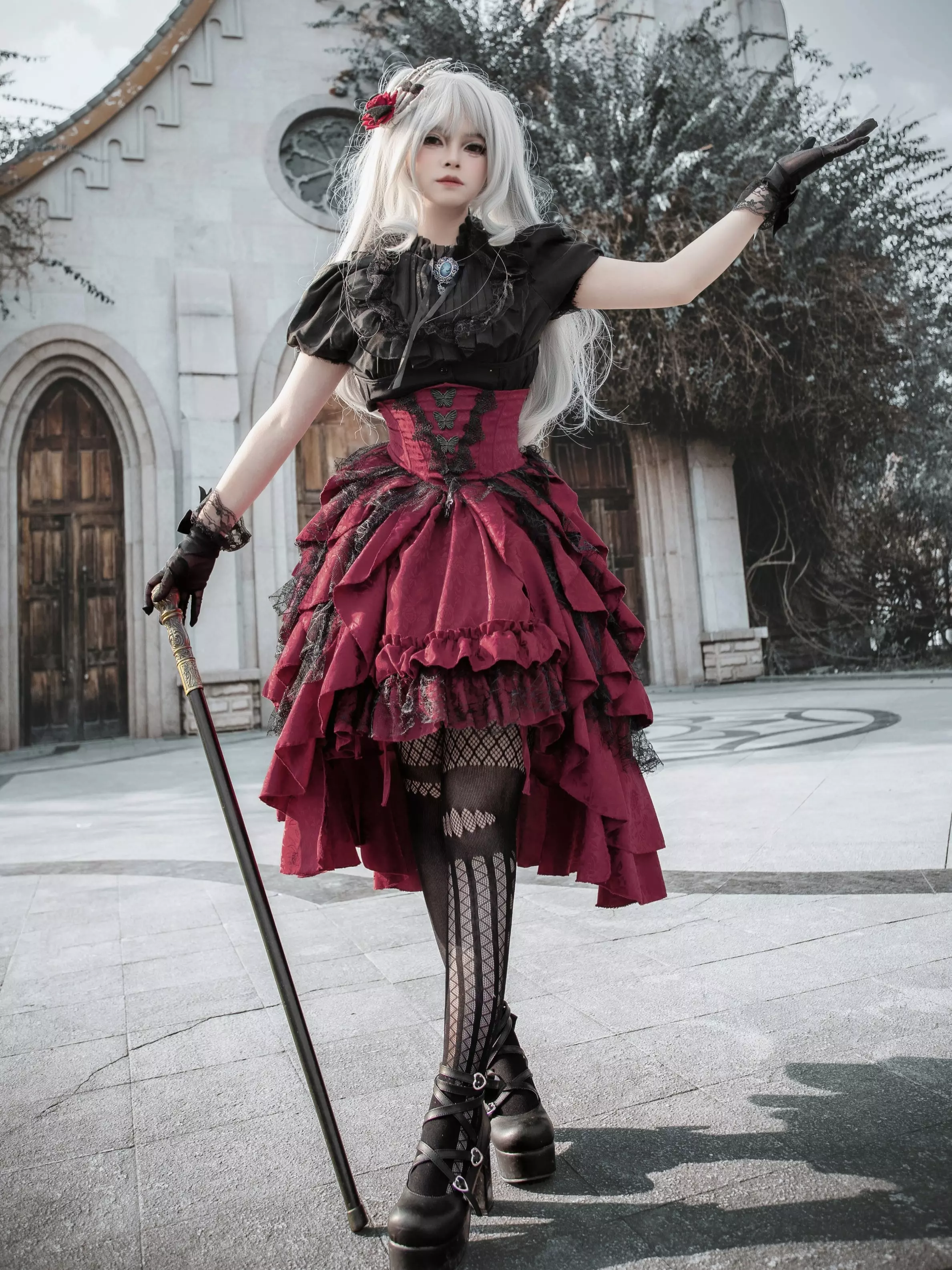 Full body gothic lolita two-piece outfit with black lace blouse, wine-red high-low ruffle skirt, fishnet stockings and platform boots, side profile