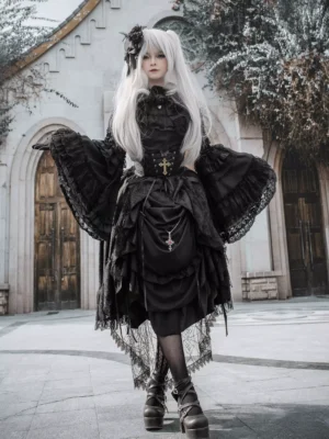 Black Gothic Lolita dress set front view featuring lace-up corset waist, bell-shaped lace sleeves, and layered ruffled skirt with high-low hem, photographed in Victorian church courtyard setting
