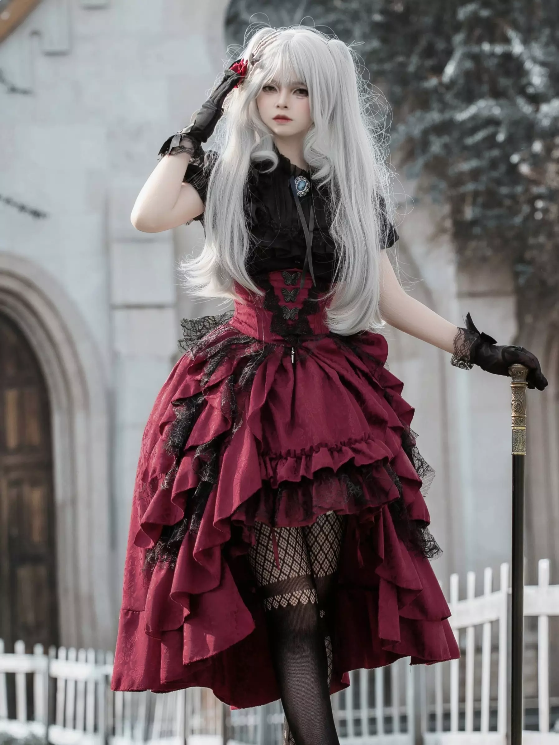 Gothic lolita two-piece dress set with black jacquard lace blouse and wine-red high-low tiered ruffle skirt worn with fishnet stockings, front three-quarter view