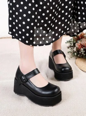 Black Mary Jane platform pumps with round toe and ankle buckle strap worn with black polka-dot midi skirt, front-side angle view showcasing matte PU leather and thick platform sole