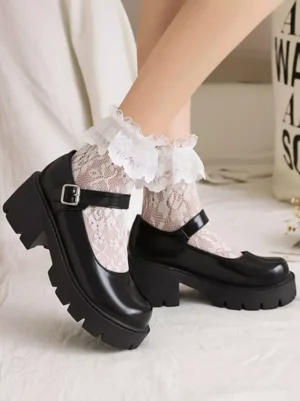 Black glossy PU leather Mary Jane platform pumps showcasing side profile with substantial block heel, metal ankle buckle strap detail, frilly lace socks styling on white bedding, side oblique overhead angle