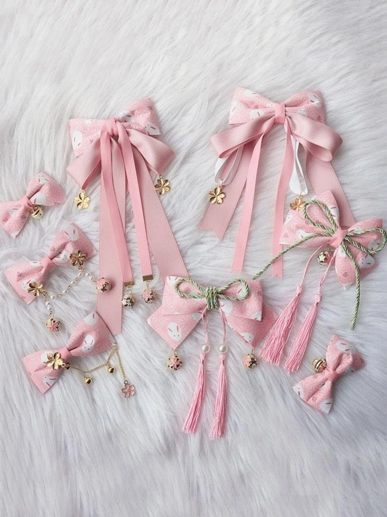 Assorted pink sakura lolita hair accessories set with satin ribbons gold charms tassels and rabbit print on white fuzzy background display