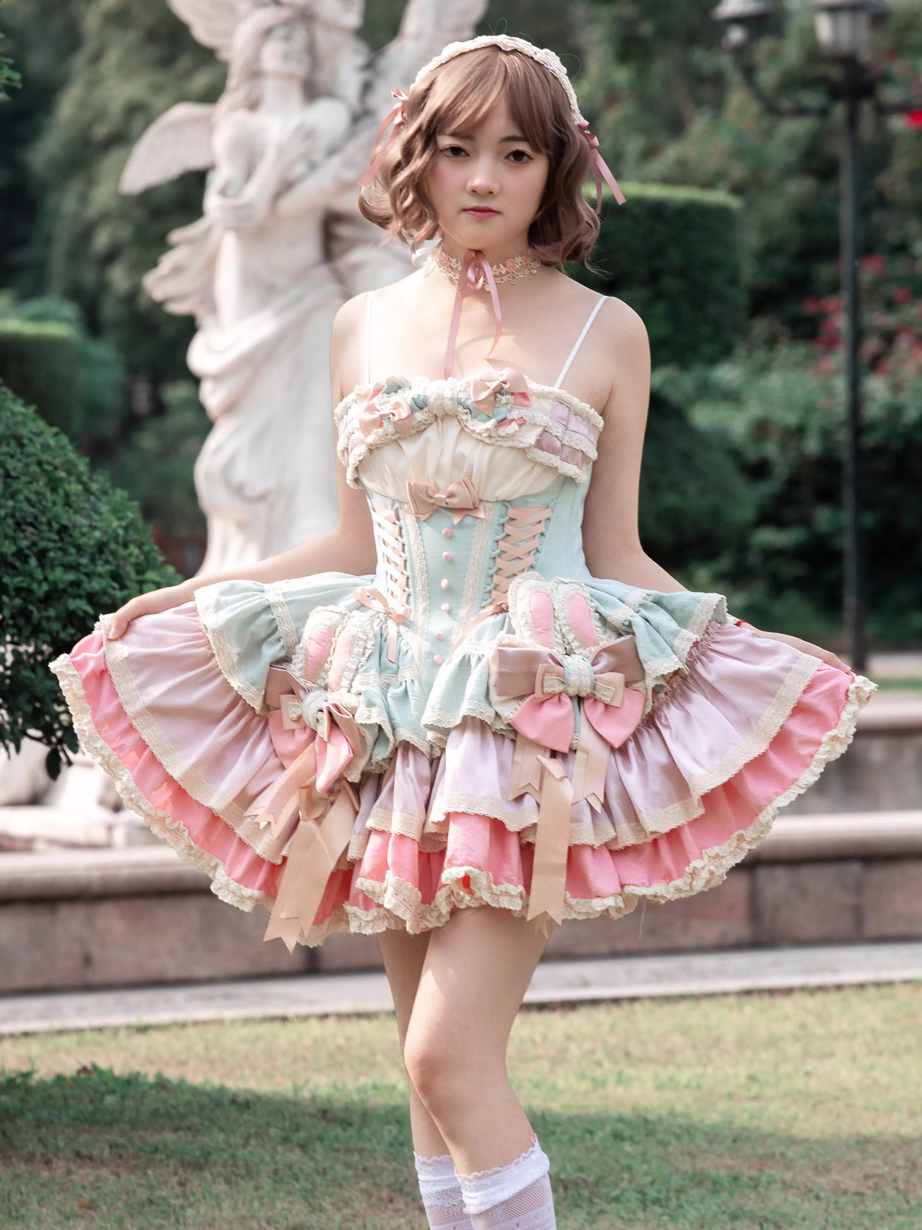 Full-length outdoor view of girl wearing sweet lolita fairy dress with white knee socks corset bodice and tiered ruffled skirt with lace trims