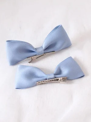 Pair of baby blue matte satin lolita bow hair clips with silver metal alligator clips flat lay top-down product photography on white background