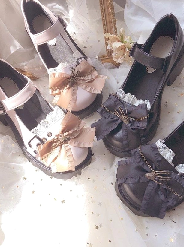 Two-tone beige and black Lolita platform shoes flat lay with satin bow, lace trim, buckle ankle strap, and thick block heel on star-patterned tulle with vintage frame