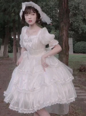 Beige cream short-sleeve Hime Lolita gown with square neckline and lace-trimmed ruffled tulle skirt, worn with wide-brimmed hat in park setting