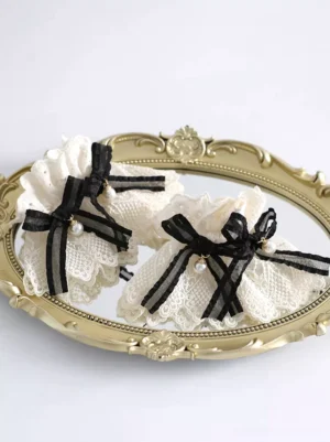 Beige ruffled lace wrist cuffs with black ribbon bows and pearl pendants in cream-black two-tone Sweet Lolita oversleeves style displayed on vintage golden carved tray