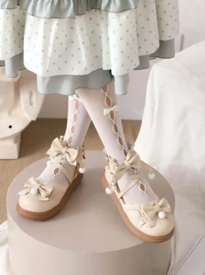 Beige lolita ankle-strap flats with round toe and cross-strap design featuring bow pom-pom accents side view display