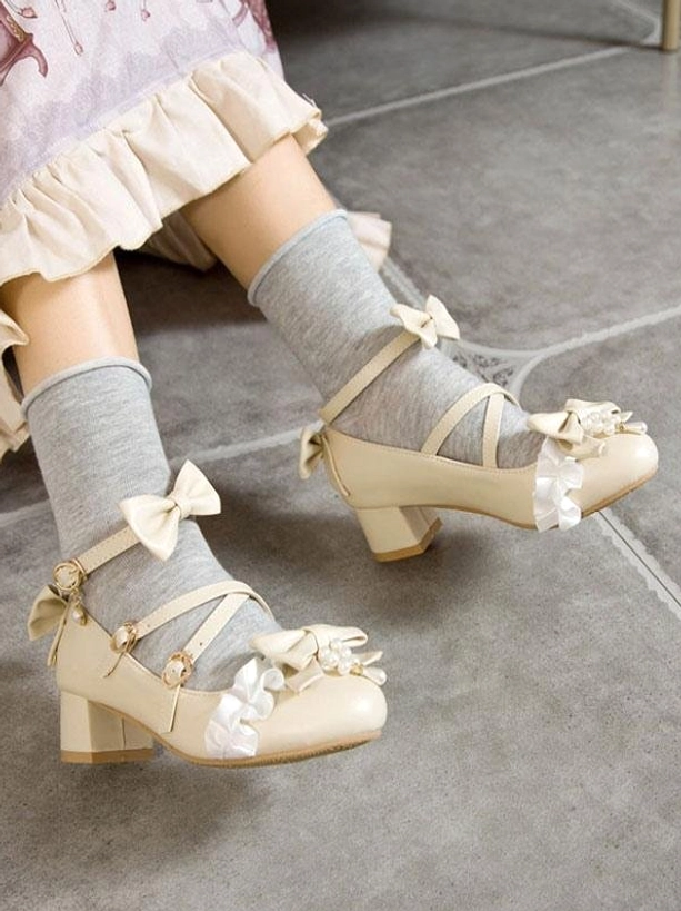 Beige lolita chunky heel pumps with bow embellishment and ruffle trim shown in side oblique view of model's feet wearing plain gray crew socks, displaying ankle buckle strap and block heel profile