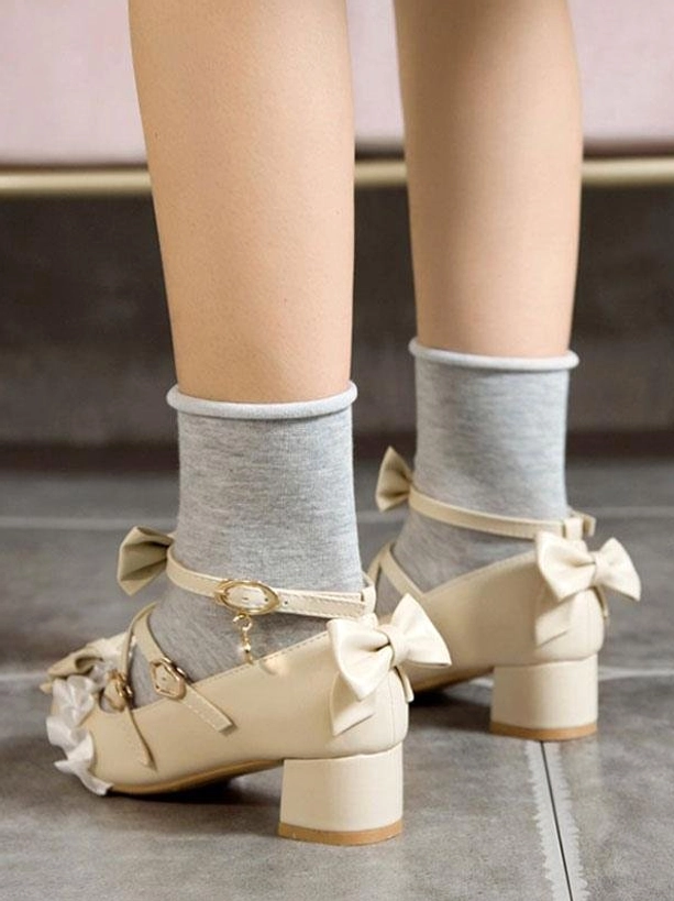 Beige lolita chunky heel pumps featuring back bow placement, ruffled toe cap and pearl accents shown from rear view of model's feet with gray crew socks, highlighting structured block heel and feminine design elements
