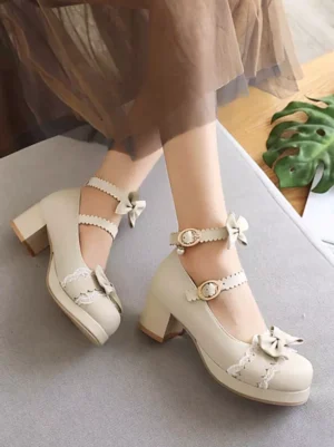 Overhead flat lay of beige lolita pumps showing bow accents, pearl buckle details, and round block heel on gray surface with plant decor