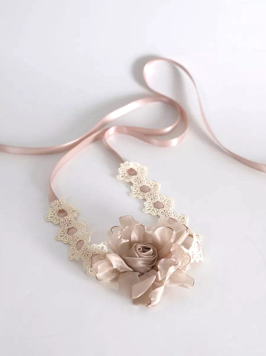 Beige floral satin rose sweet lolita choker flat lay top-down view showing hollow lace trim framework, pink satin tie closure straps, and 3D fabric rose decoration on neutral white background