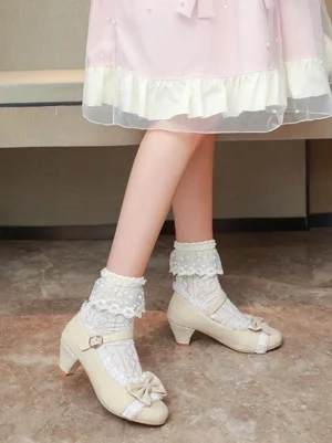 Beige suede Lolita Mary Jane shoes with bow decoration on-foot side view worn with pink ruffle dress and lace socks, round block heel detail on indoor bench
