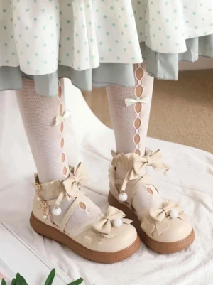 Beige sweet lolita flat shoes with pom-pom bow detail and ruched leather upper worn with polka-dot frilly dress and hollow-out stockings front view