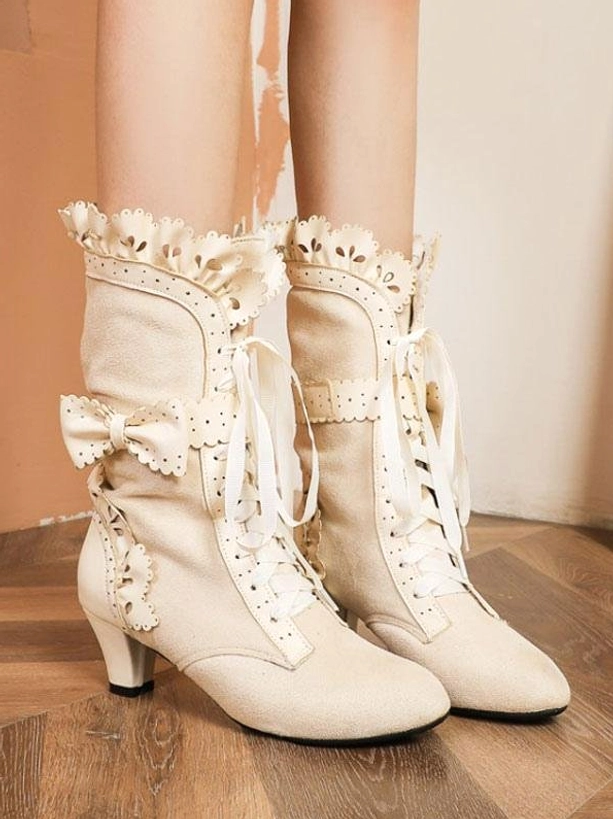 Beige lolita kitten heel boots with ruffled lace trim and side bow detail worn on wooden floor front view
