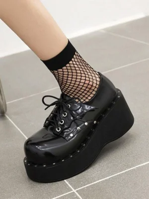 Black lolita shoes side profile view showing thick wedge sole chunky platform and polished round toe with fishnet socks indoor tiled setting