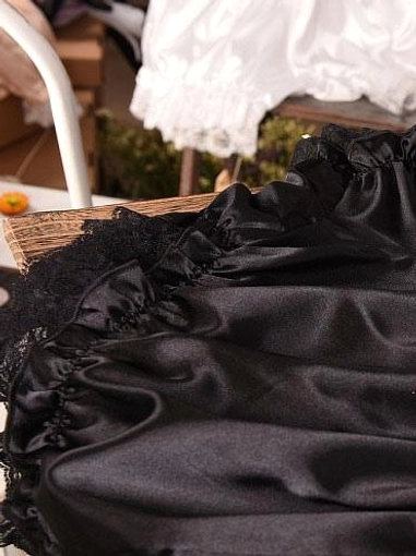 Close-up detail of black lolita bloomer lace ruffle edge on wooden table, showcasing soft wrinkled satin fabric texture and delicate lacework craftsmanship