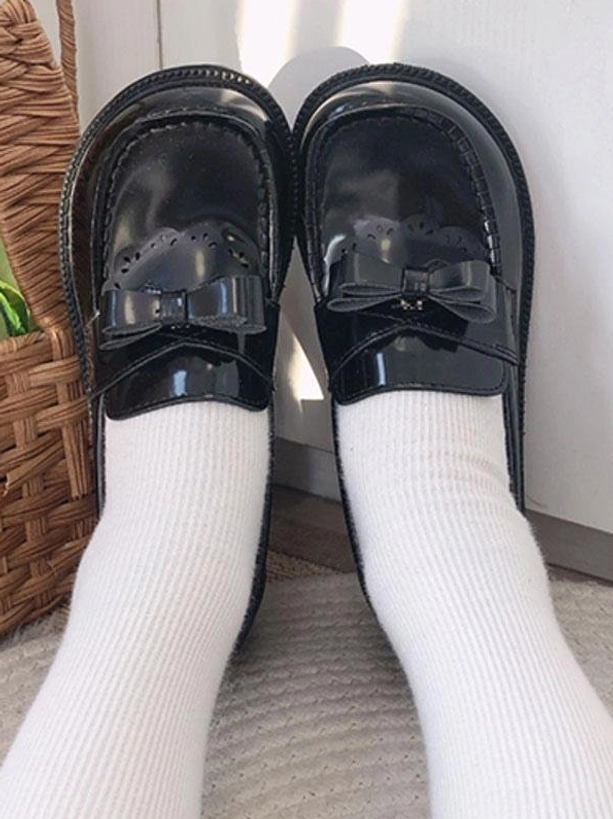 Pair of black patent leather bow loafers flat lay top view with white ribbed socks and wicker basket, academic lolita shoes