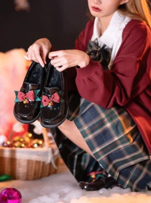 Classic black lolita bow pumps with red-green bow and bell charm front overhead display held by model wearing red cardigan and plaid skirt showing glossy pu leather round toe