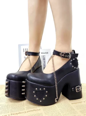 Model wearing black lolita platform pumps with chain trim and heart studs front three-quarter worn view newspaper background styled lolita coordinate ankle buckle strap