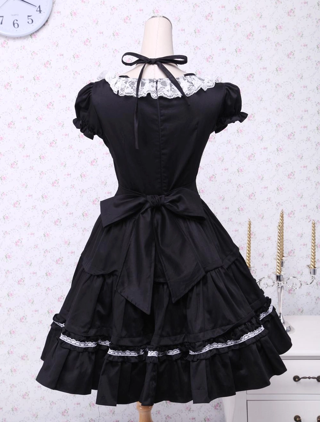 Black classic lolita dress rear back view displaying large waist bow, crisscross neck strap, and architectural layered lace skirt design