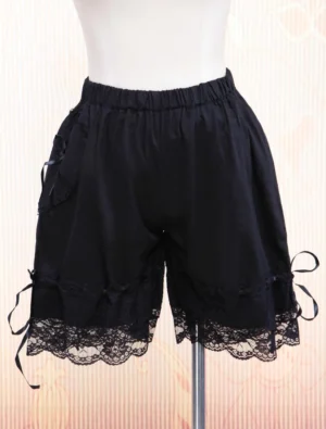 Black cotton lolita bloomers front three-quarter view showing elastic waist, delicate lace hem trim, and side ribbon accents on dress form with patterned backdrop