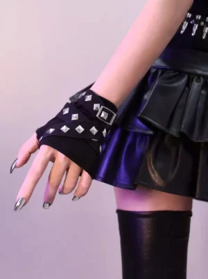 Single black gothic wrist cuff accessory featuring silver pyramid rivets and metal buckle closure, styled with pleated leather skirt and thigh-high boots, close-up wrist detail