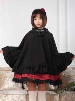 Black gothic hooded lolita cape coat with ruffled hem worn by female model in full-body front view over red lolita skirt and white stockings