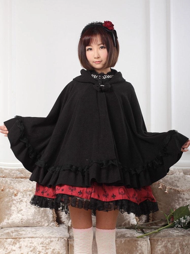 Black gothic hooded lolita cape coat with ruffled hem worn by female model in full-body front view over red lolita skirt and white stockings