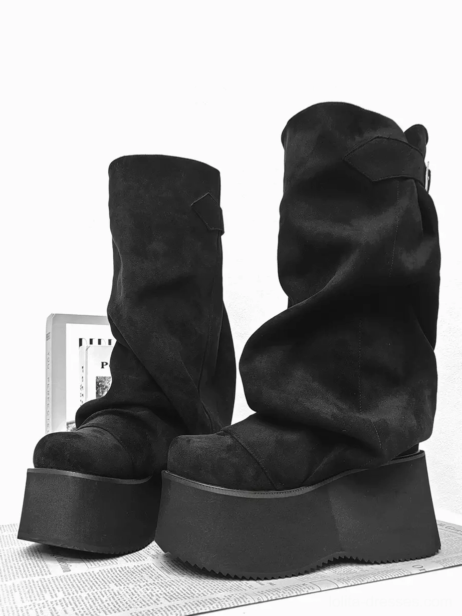 Pair of black slouchy platform mid-calf gothic lolita boots front three-quarter view on newspaper background, showing thick platform sole, matte black corduroy finish, and slouchy shaft
