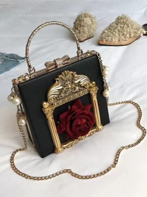 Black gothic lolita box handbag with golden carved frame, red rose and pearl chain accents, styled flat lay with fuzzy slippers on bedsheet background