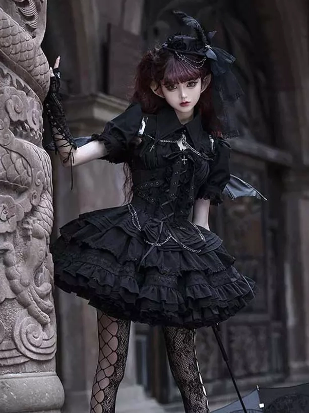 Black gothic lolita jumper dress with fishnet stockings chain decorations and tiered ruffled skirt worn in vintage stone carving scene