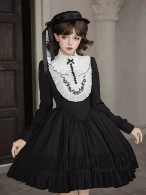 Black Gothic Lolita dress with long sleeves and tiered ruffled skirt, worn with black mini hat and white embroidered detachable collar, front three-quarter view on female model