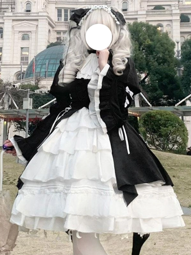 Front three-quarter mannequin view of black gothic lolita dress featuring tiered ruffled white skirt, lace-up black bodice, and large bow collar