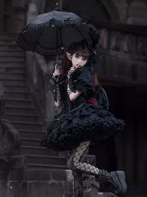 Black gothic lolita dress with tiered ruffled skirt and fishnet stockings worn by female model with parasol dark stairwell full body view