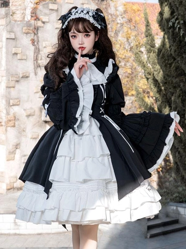 Three-quarter front view of gothic lolita dress displaying flared long sleeves with white trim, front ruffled bib, and asymmetrical black overskirt