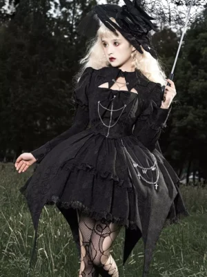 Black gothic lolita dress with tiered ruffled skirt and cross chain trim details, front full-body view worn by blonde model in outdoor forest setting