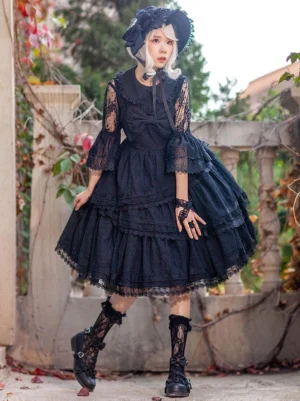 Black gothic lolita JSK dress full front view on female model with lace flared sleeves tiered skirt and oversized front bow outdoor styling